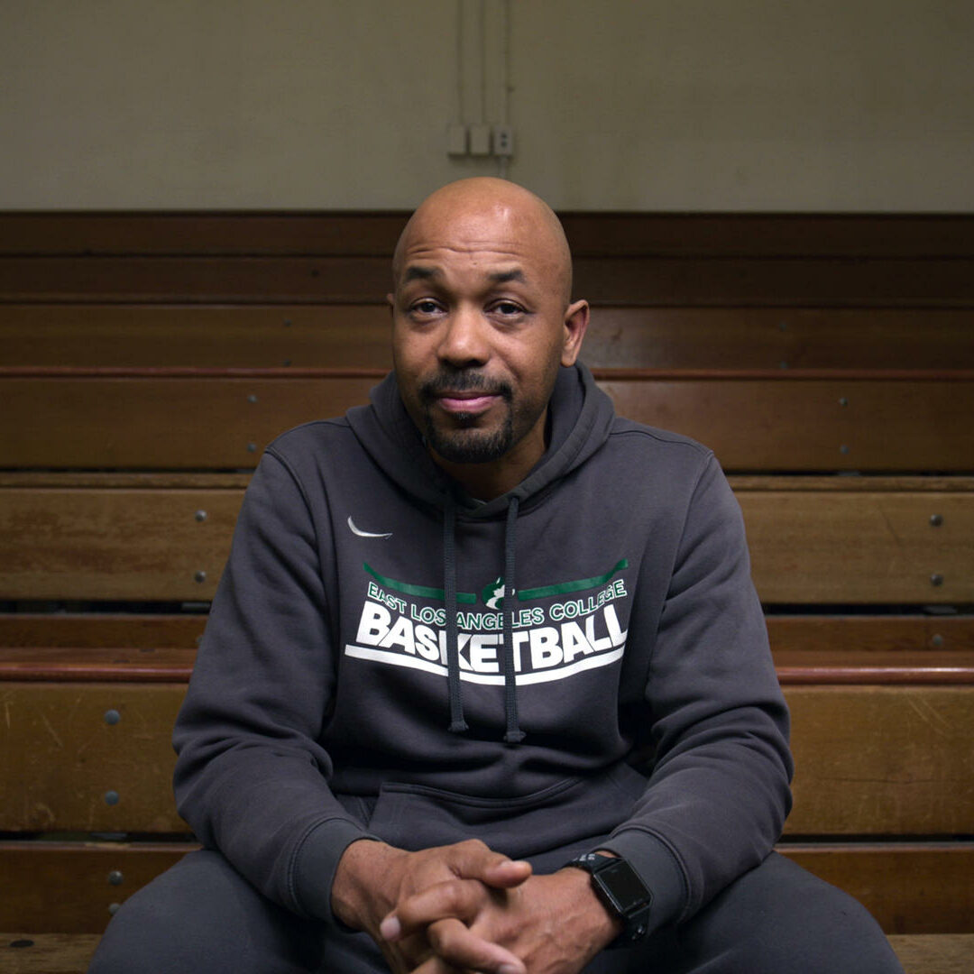 Coach John Mosley sitting in the first row of arena bleachers